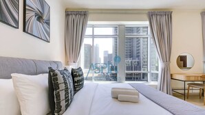 Une chambre d’hôtel avec un lit, un bureau, une chaise, une fenêtre avec des rideaux et une vue sur la ville.