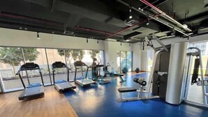 Une salle de sport équipée de tapis de course, d’un rameur et d’un banc de musculation.