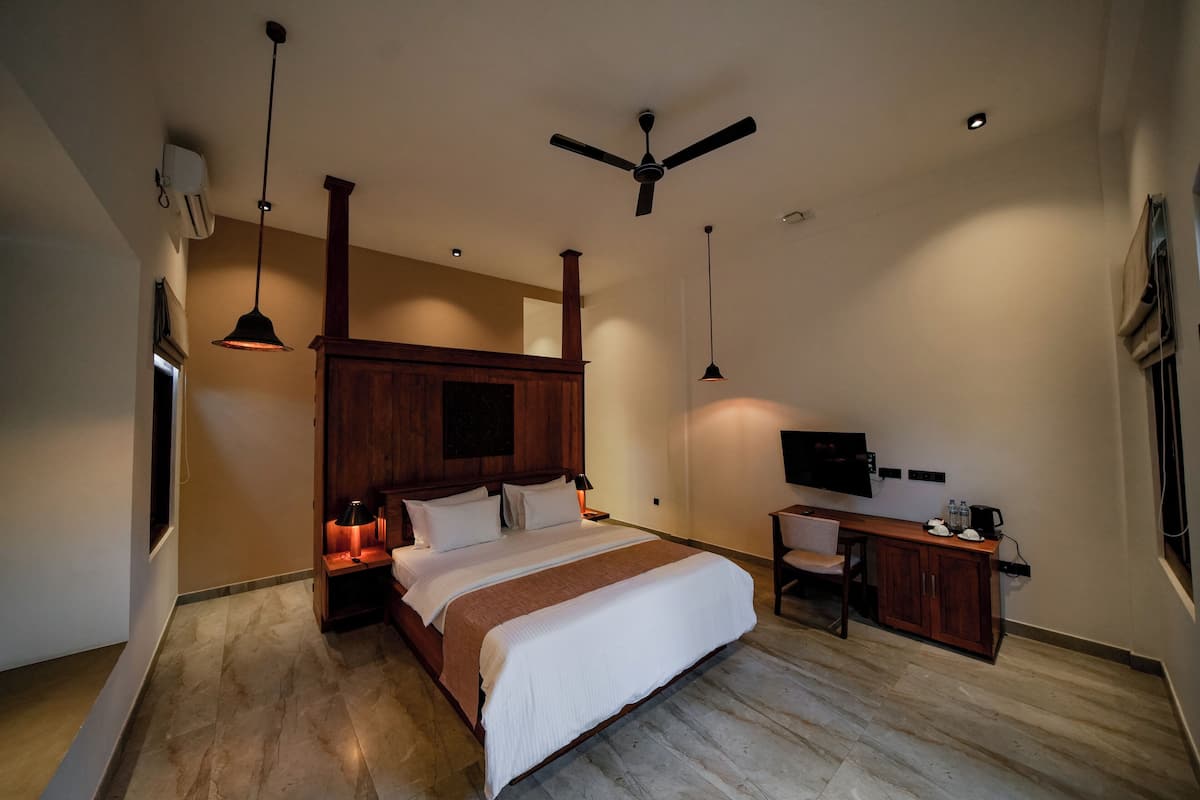 A modern bedroom with a large bed, a desk, a chair, a ceiling fan, and a TV.