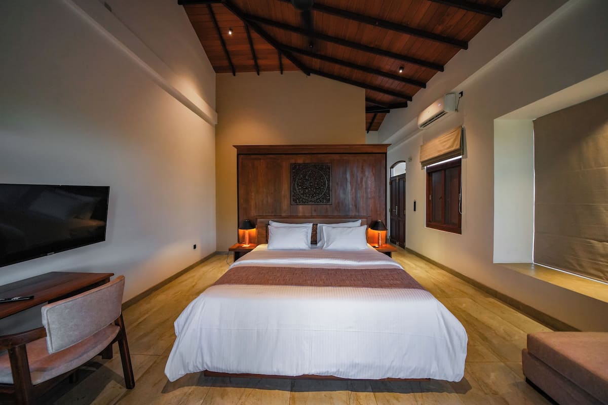 A spacious bedroom with a large bed, a flat-screen TV, a wooden headboard, and a small seating area.