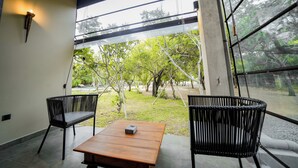 A modern interior with a wooden table and two wicker chairs, large windows with a view of greenery outside. - Adaar Kuchchaveli (Trincomalee)