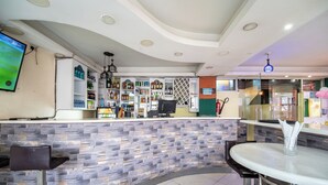 A modern bar area with a stone wall, a round table, and a variety of bottles on shelves. - Capital Comfort Hotel (Nairobi)