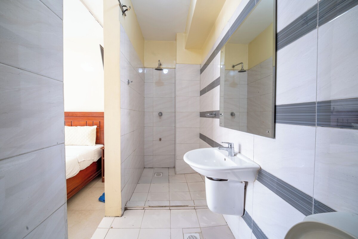 A bathroom with a shower, sink, and a bed in the adjacent room.