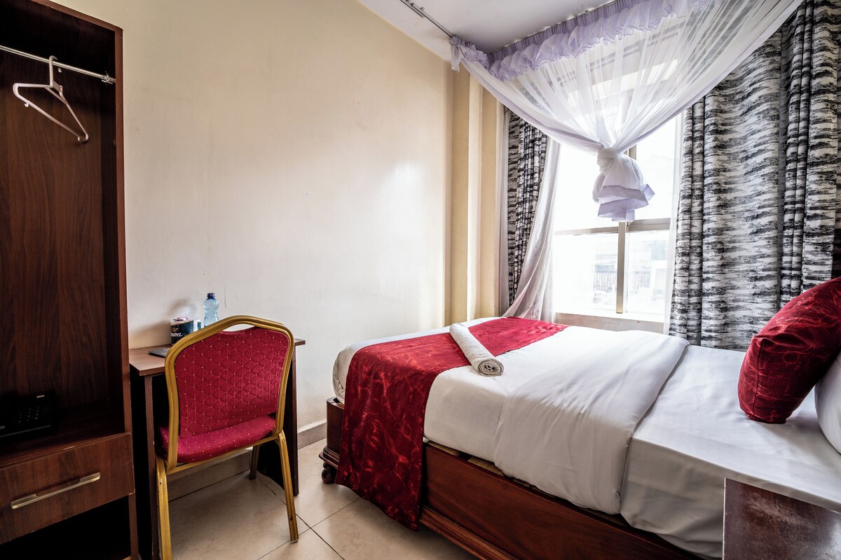 A hotel room with a bed, a desk, a chair, and a wardrobe.