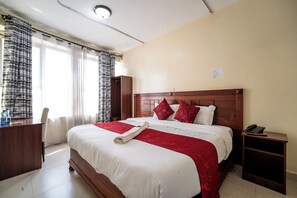 Una cama bien hecha con una colcha roja y blanca, un cabecero de madera y una mesita de noche con un teléfono.