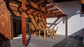 Una estructura de pérgola de madera con una mesa, sillas, una ventana y una puerta que da a un espacio interior.