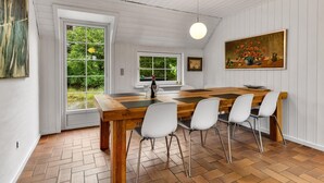 A dining area with a wooden table, white chairs, and a painting on the wall. - Cozy home in Blåvand with sauna (Blåvand)