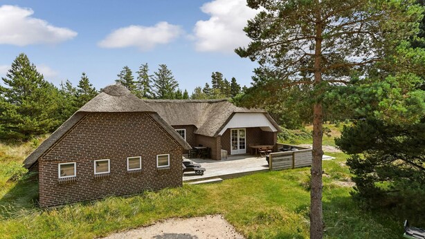 A rustic cabin with a thatched roof, a wooden deck, and a small outdoor seating area. - Cozy home in Blåvand with sauna (Blåvand)