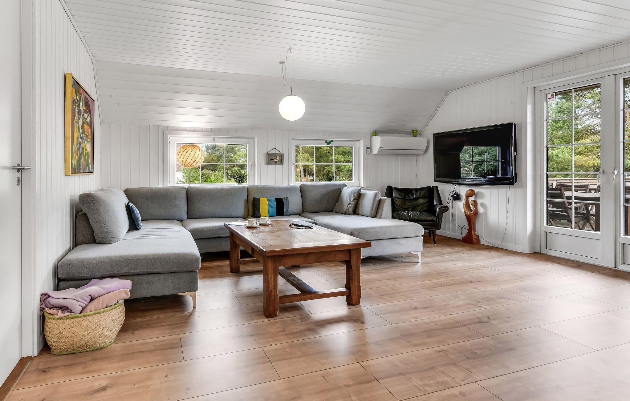 A modern living room with a grey sectional sofa, a wooden coffee table, and a flat-screen TV mounted on the wall.