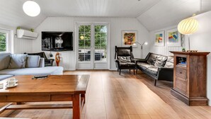 A spacious living room with a wooden floor, a large TV mounted on the wall, a leather sofa, a wooden coffee table, and a cabinet. - Cozy home in Blåvand with sauna (Blåvand)
