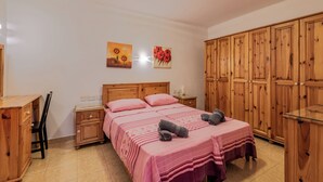 Ein Schlafzimmer mit einem Holzschrank, einem Bett mit rosa Bettwäsche und zwei Bildern an der Wand.