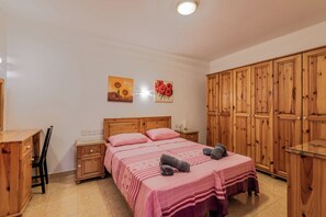 A bedroom with a wooden wardrobe, a bed with pink bedding, and two paintings on the wall. - GetawaysMalta - Harbour Lights Seafront in  St Paul's Bay LLet (St Paul's Bay)