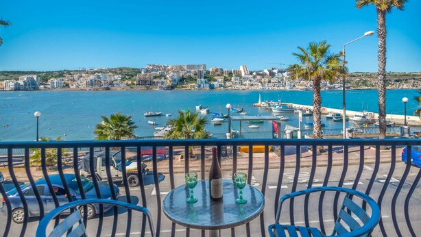 Ein Balkon mit Tisch und Stühlen mit Blick auf einen Hafen voller Boote und Gebäude.