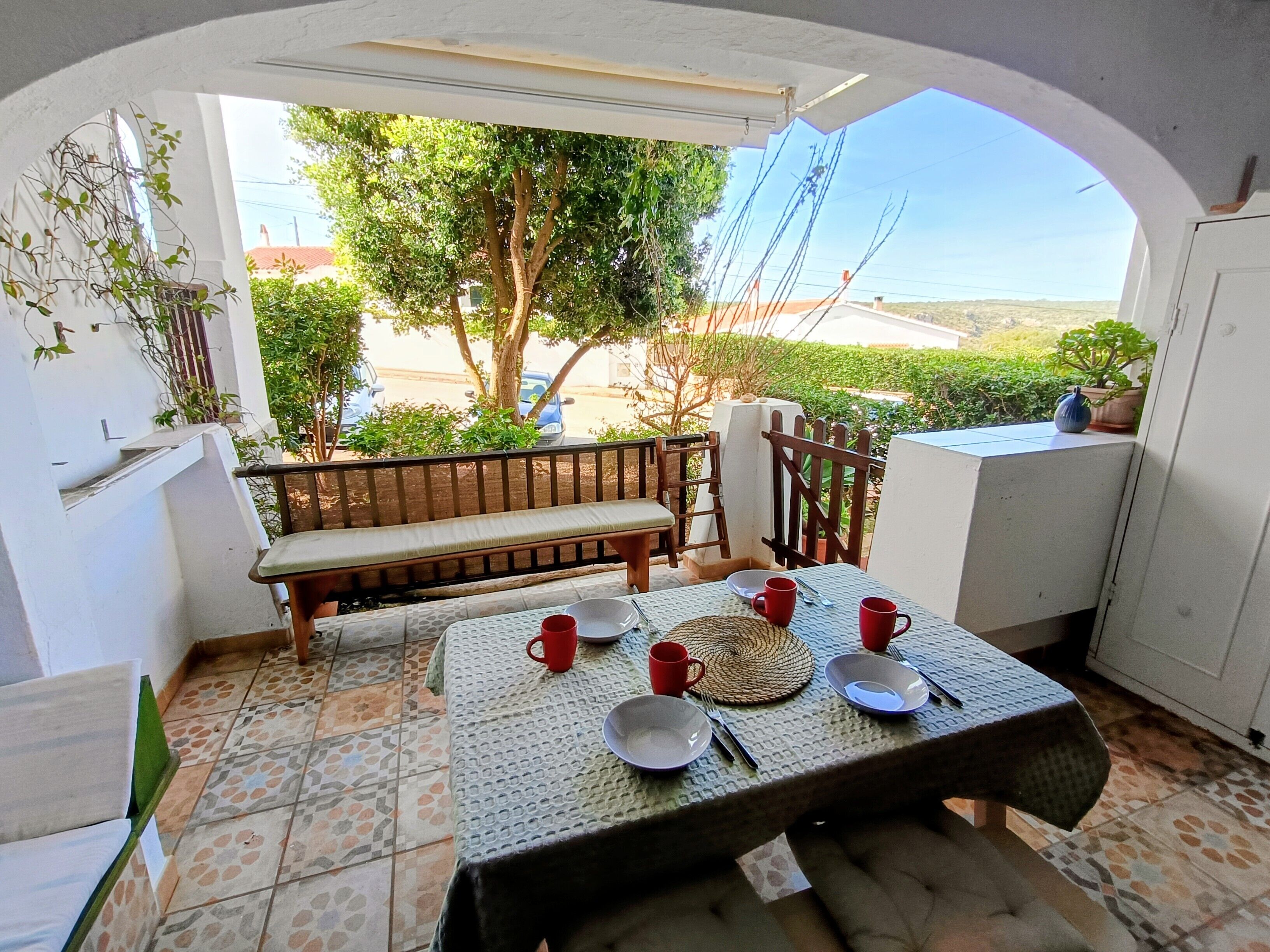 A patio with a table set for two, a bench, and a view of the outdoors.