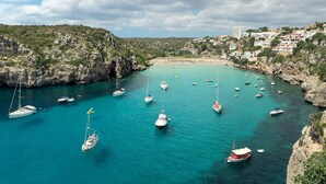 Una bahía costera con numerosos barcos, acantilados rocosos y una playa con edificios al fondo.