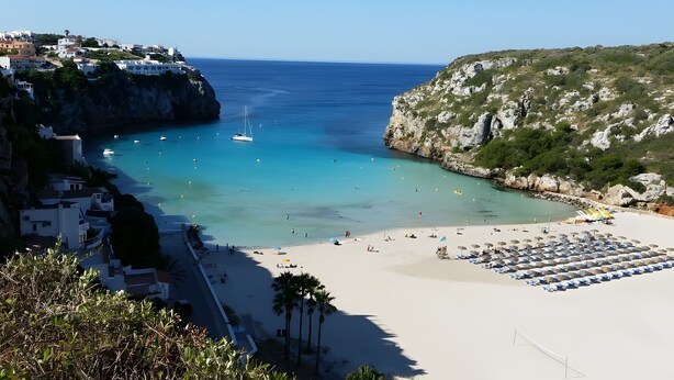 Una playa costera con vista despejada al mar, arena y un acantilado rocoso.