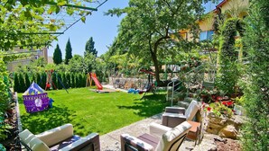 A backyard with a grassy lawn, a swing set, a slide, and a playhouse.