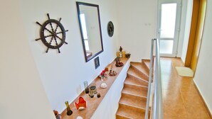 A staircase with a handrail, a wall-mounted ship's wheel, a mirror, and a shelf with various decorative items.