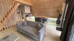 A modern living room with a grey sofa, wooden staircase, and a dining area with chairs and a table. - AFORREST FAMILY RESORT (Qusar)