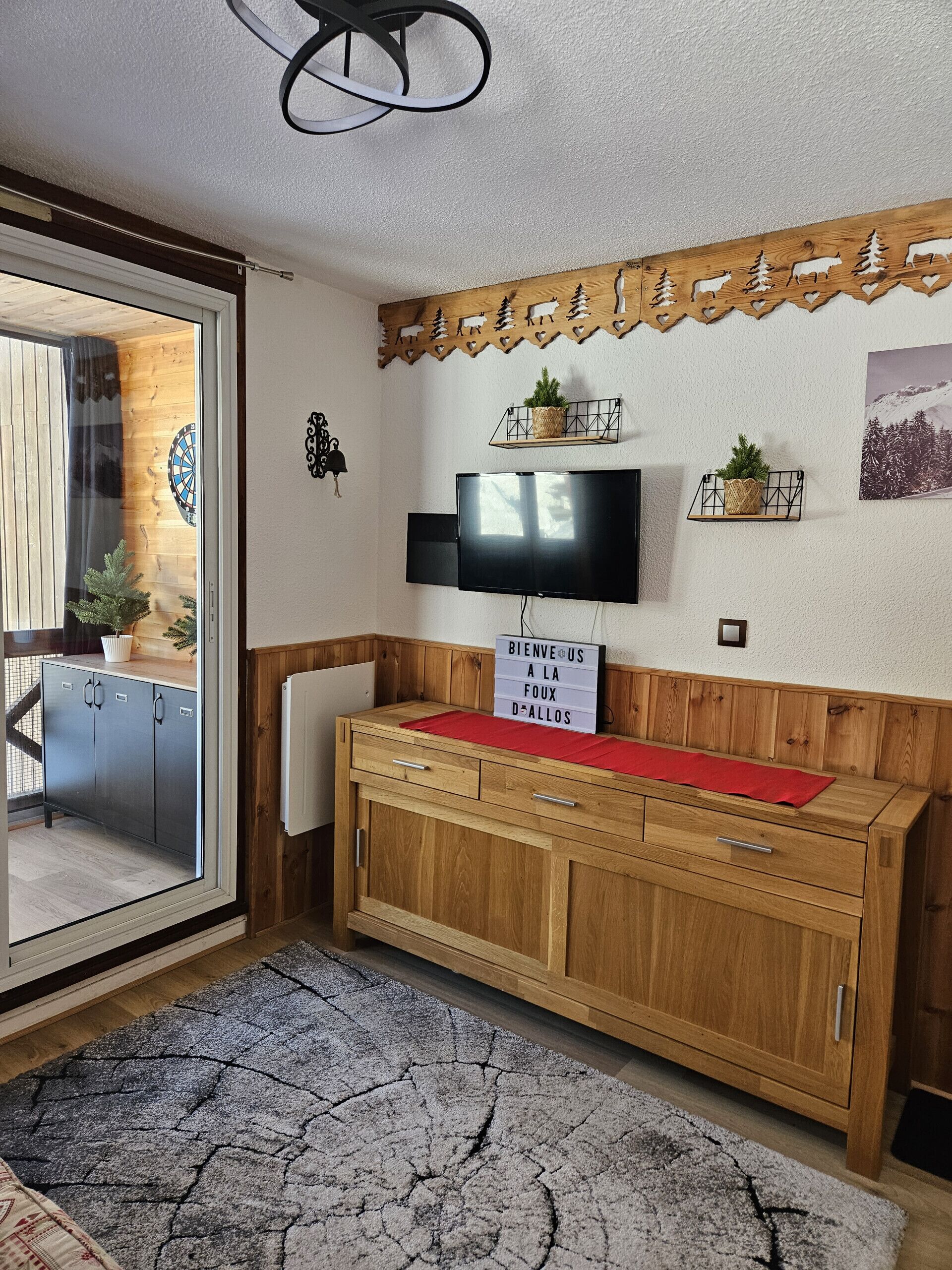 A room with a wooden cabinet, a flat-screen TV, a welcome sign, and a decorative wooden panel with animal cutouts.