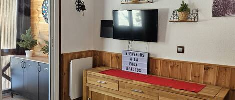 A room with a wooden cabinet, a flat-screen TV, a welcome sign, and a decorative wooden panel with animal cutouts.