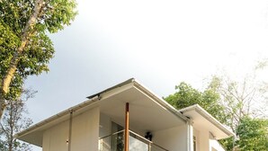 Une maison moderne à deux étages, dotée d’un balcon au niveau supérieur et entourée de verdure.