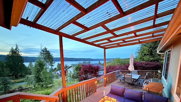 A wooden deck with a glass ceiling, outdoor seating, and a view of a lake.