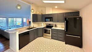 A modern kitchen with dark cabinets, a black refrigerator, a microwave, and a stove.