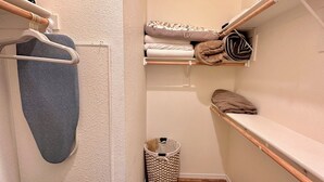 A small, narrow closet with wooden shelves, a hanging rack, and a storage basket.