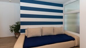 Ein Zimmer mit einem Bett an einer Wand mit blauen und weißen Streifen, einem Fenster und einer Topfpflanze.