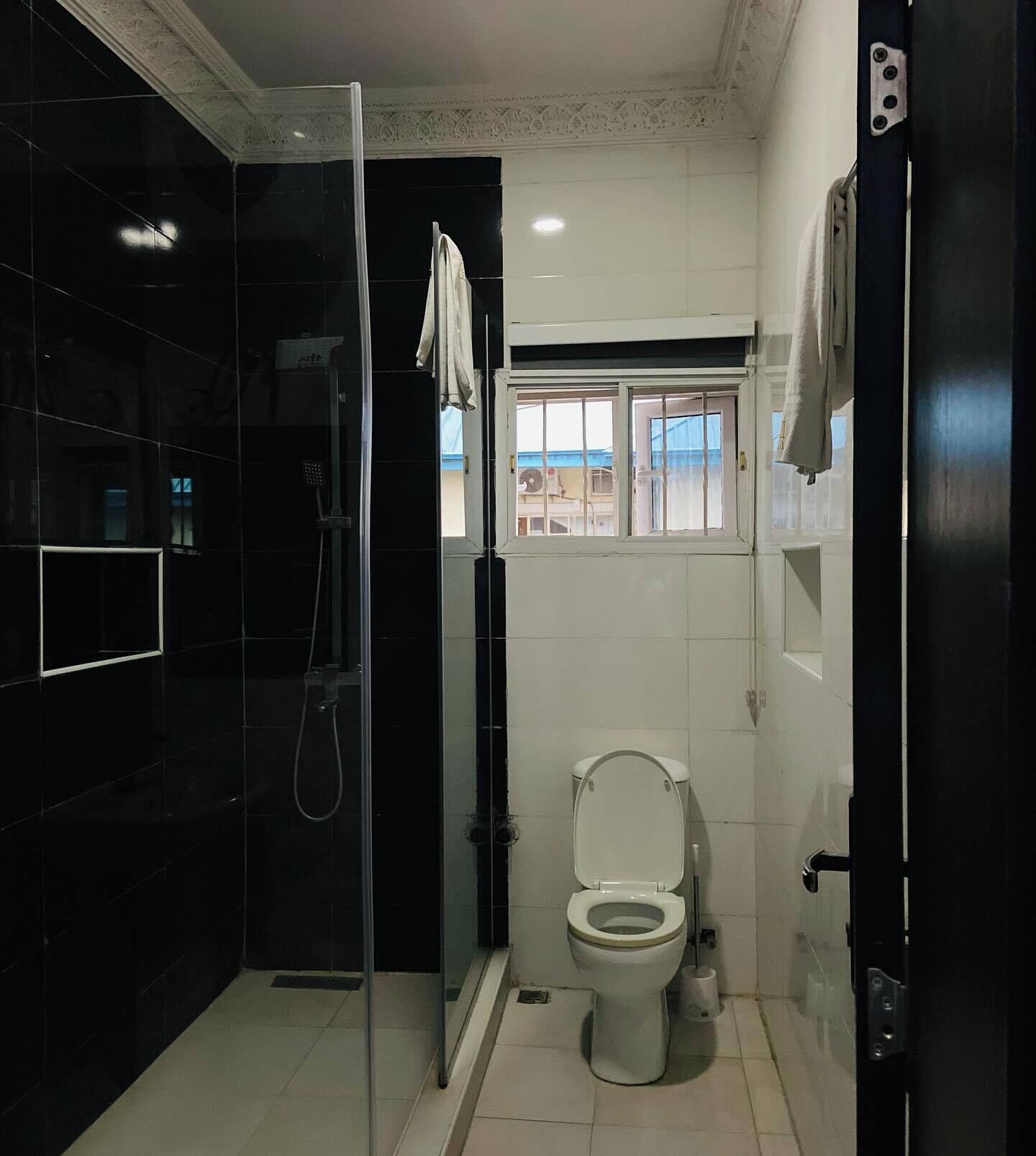 A modern bathroom with a glass-enclosed shower, a toilet, and a window providing a view of the outside.