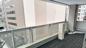 A balcony with a wooden floor, metal railing, and a view of a cityscape. - Fierement inn (Sapporo)