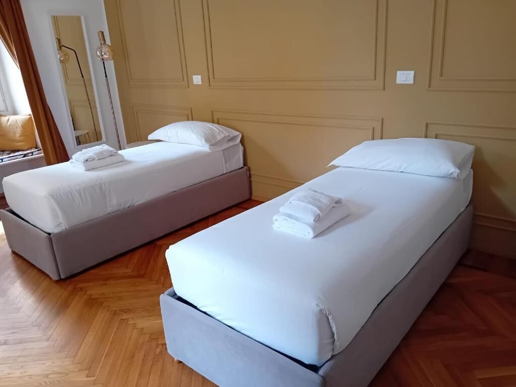 Ett hotellrum med två separata sängar, trägolv och en spegel på väggen.