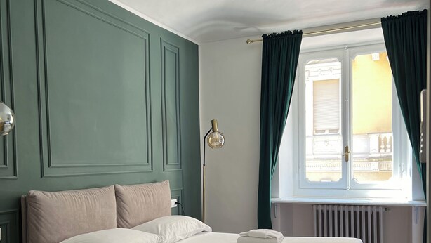 A neatly made bed with pillows and folded towels, a bedside table, a floor lamp, and a window with curtains. - Turin Central Suite (Turin)