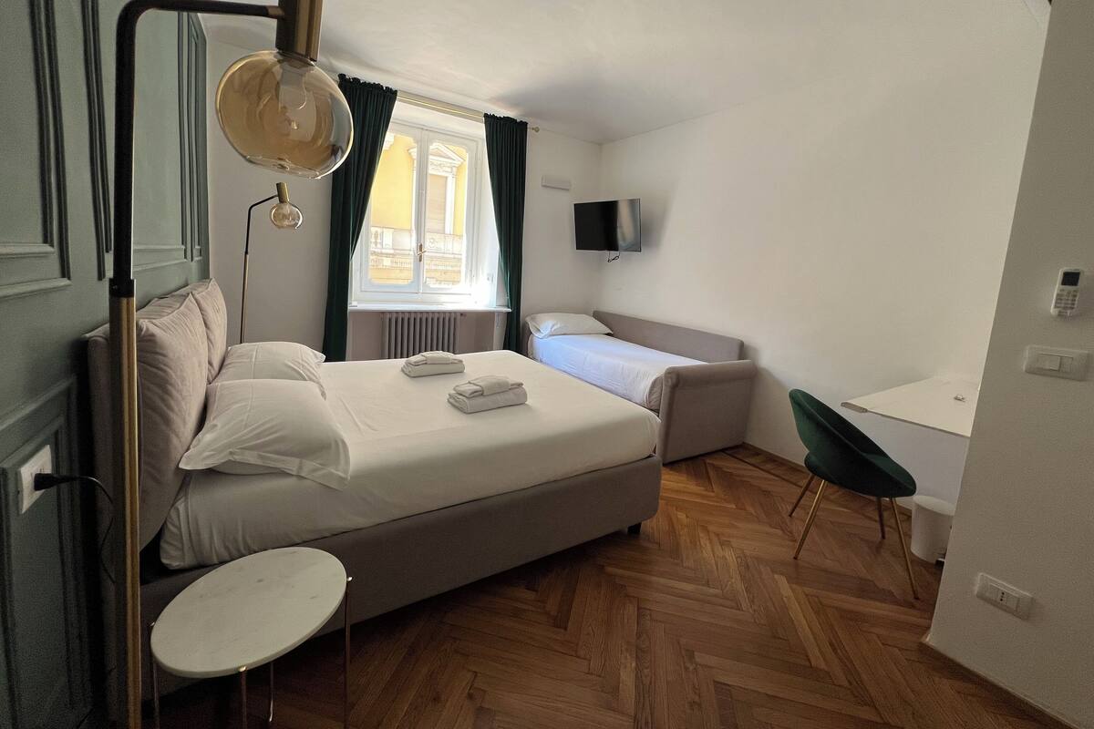 A modern hotel room with a large bed, a small round table, a desk, and a TV mounted on the wall.