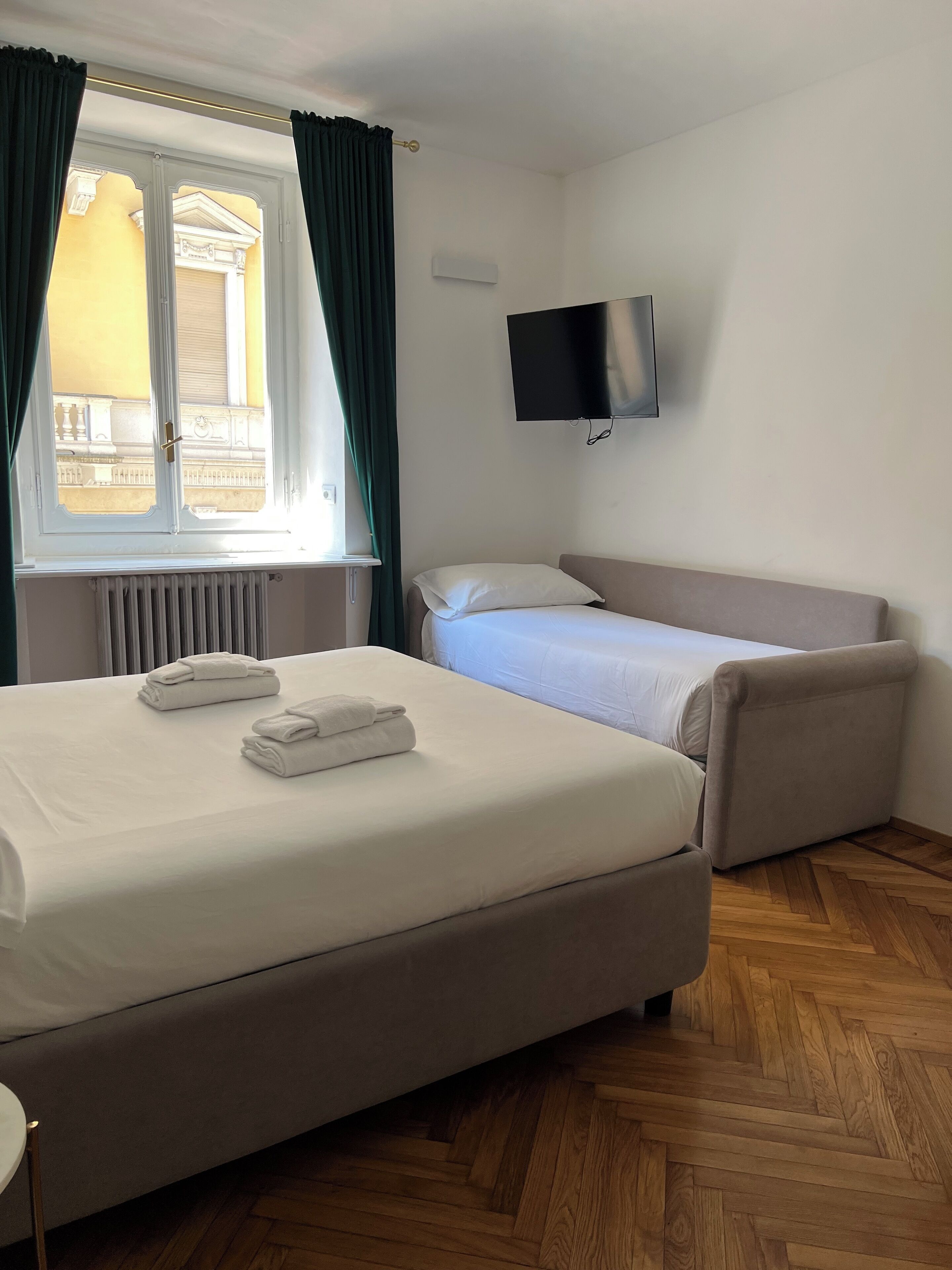 Ein Hotelzimmer mit einem Bett, einem Sofa, einem an der Wand montierten Fernseher und einem Fenster mit Vorhängen.