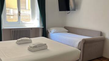 Ein Hotelzimmer mit einem Bett, einem Sofa, einem an der Wand montierten Fernseher und einem Fenster mit Vorhängen.