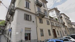 A multi-story building with balconies, a visible ground floor entrance, and a parking sign. - Turin Central Suite (Turin)
