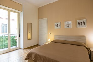 A bedroom with a bed, a nightstand, a lamp, and a sliding glass door leading to a balcony. - Cozy Escape by Napoliapartments (Naples)