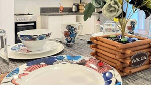 A dining area with a table set for two, featuring floral-patterned plates and a centerpiece with yellow flowers and a wooden box labeled "Feliz Dia".