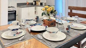 A dining area with a wooden table set for four, surrounded by white cabinets and a kitchen in the background.