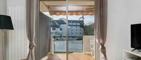 Una habitación con puerta corrediza de vidrio que da a un balcón, una cama, una silla y un televisor.