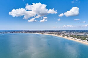 Un paysage urbain côtier avec une vaste plage, un ciel dégagé et quelques nuages épars.