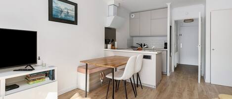 Una cocina moderna con armarios blancos, una mesa de comedor de madera y un televisor sobre un soporte blanco.