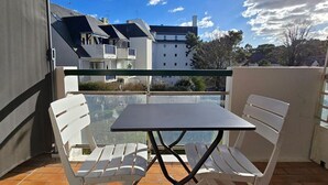 En balkon med et bord og stole, et frit udsyn til bygninger i baggrunden, og et flisegulv.