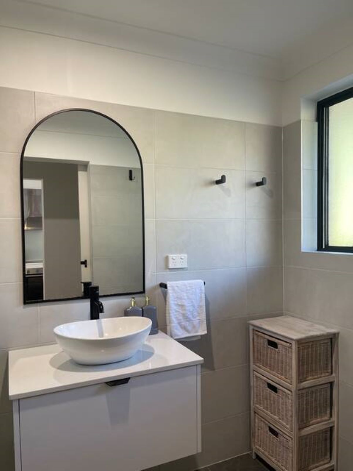 Une salle de bain avec un meuble-lavabo blanc, un grand miroir, un porte-serviettes et un panier en osier.
