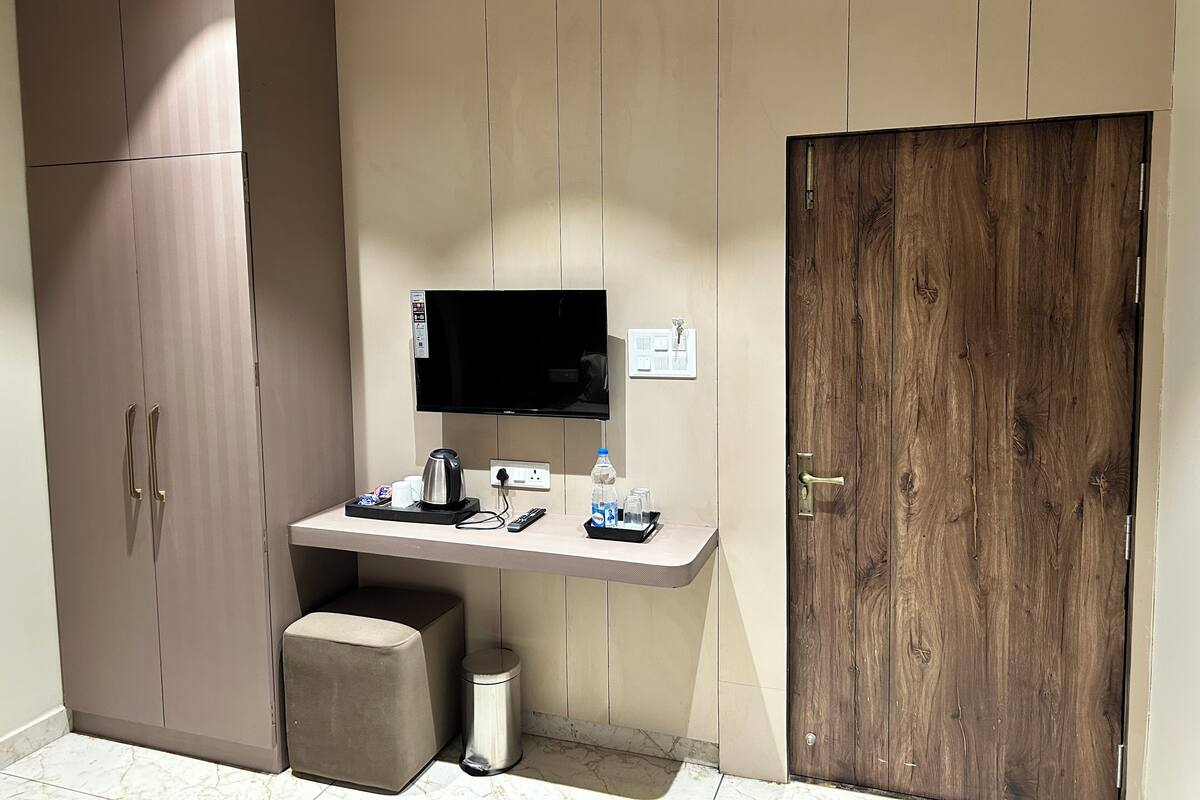 A compact room with a kitchenette, a flat-screen TV, a wooden door, and a marble floor.