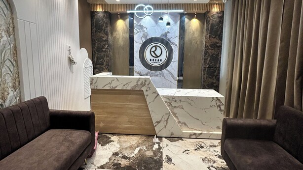 Un hall d’entrée moderne avec un sol en marbre, deux canapés, un ventilateur de plafond et un comptoir de réception orné d’un logo.