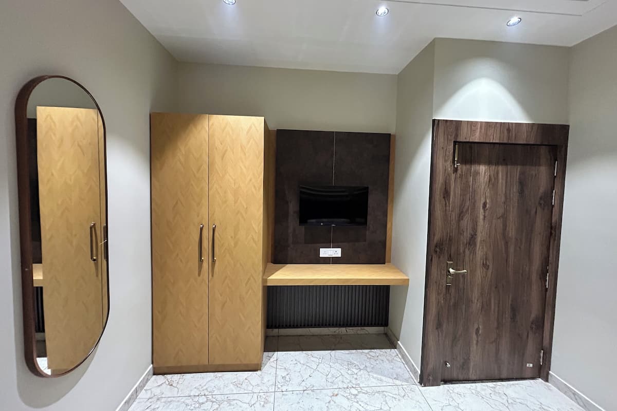 A room with a wooden wardrobe, a built-in TV shelf, and a wooden door.