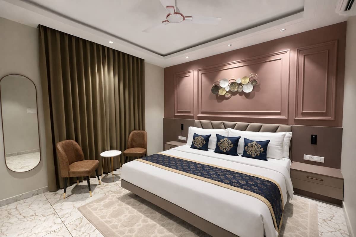 A modern bedroom with a large bed, two chairs, a small table, and a decorative wall panel.